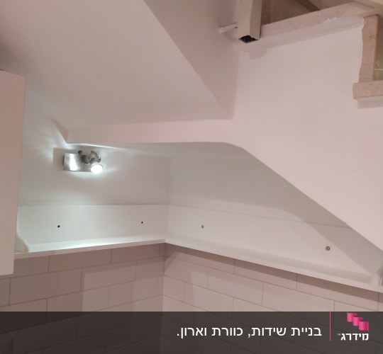 מדף עץ מותקן בפינת קיר מתחת למדרגות